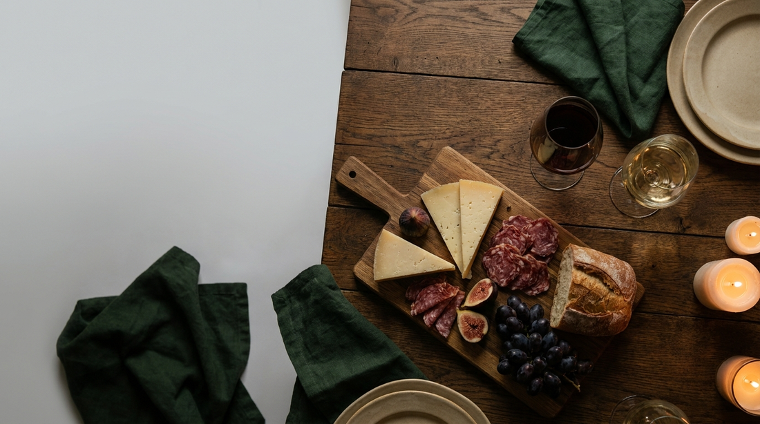 A charcuterie and cheese board with figs, grapes and glasses of red and white wine on a dark oak table