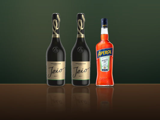Two bottles of Bisol Jeio Prosecco and a bottle of Aperol on a dark bar top